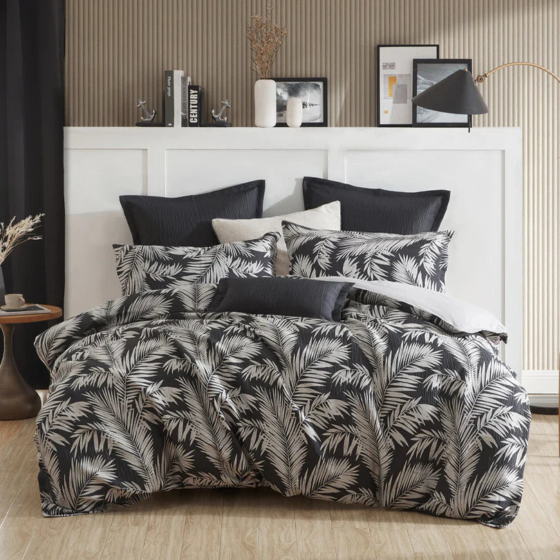 Transform your bedroom into a modern oasis with the Logan and Mason Platinum Villa Quilt Cover Set Range in Black. This exquisite collection weaves shadowy palm motifs, in a monochrome palette of black and silver, to create a texturally rich and tropical ambiance that is truly delightful.